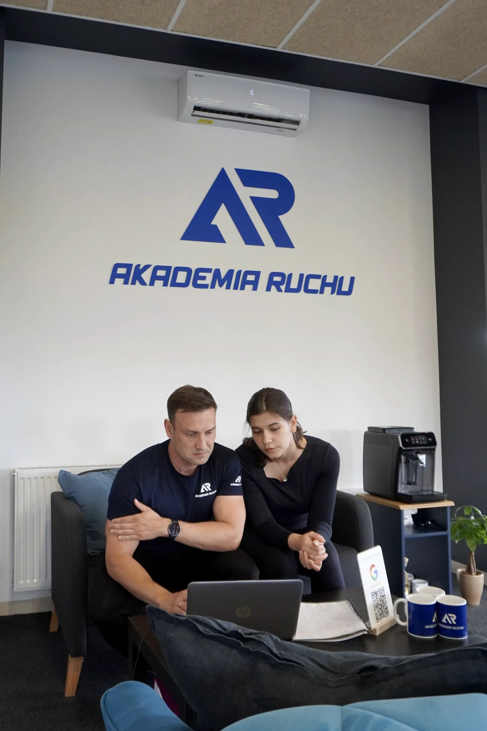 Trenerzy Akademii Ruchu przy laptopie w strefie recepcyjnej, pod logo studia